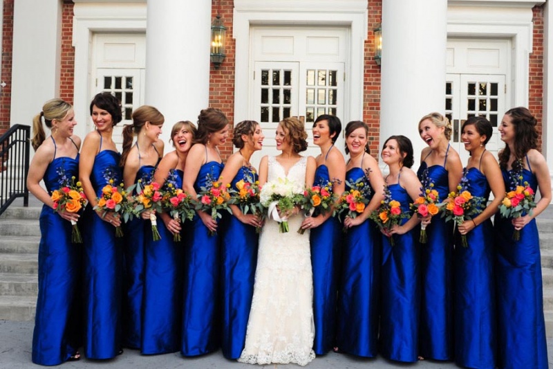 mxcp46-bridesmaids-looking-at-bride-smiles-laughing-holding-bouquets-outside-church